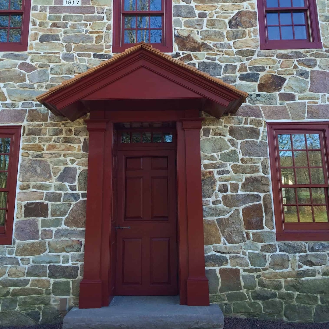 the entrance of an old stone building with burgundy red trim along the windows and a red front door