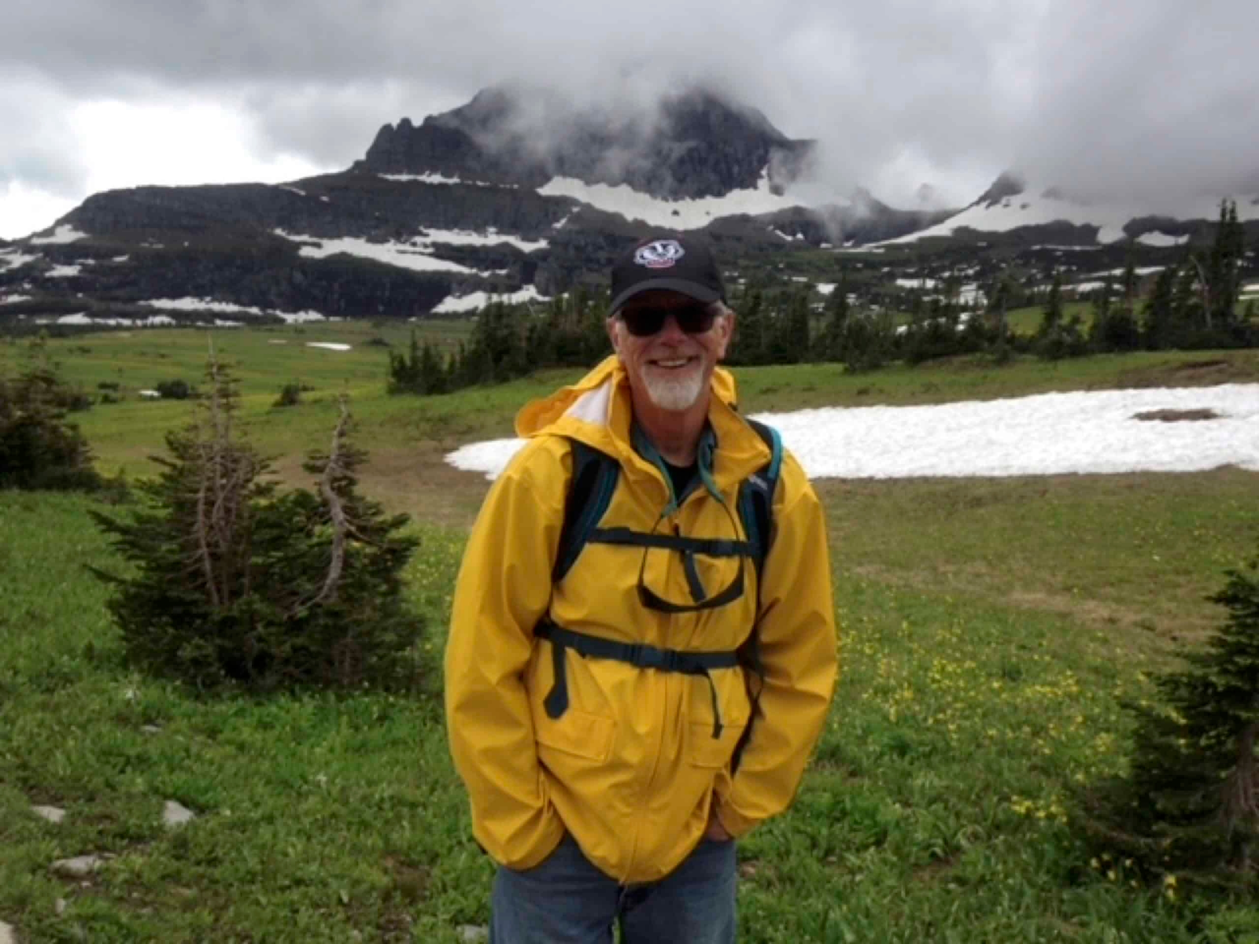 man in yellow jacket posing with a mountain behind him