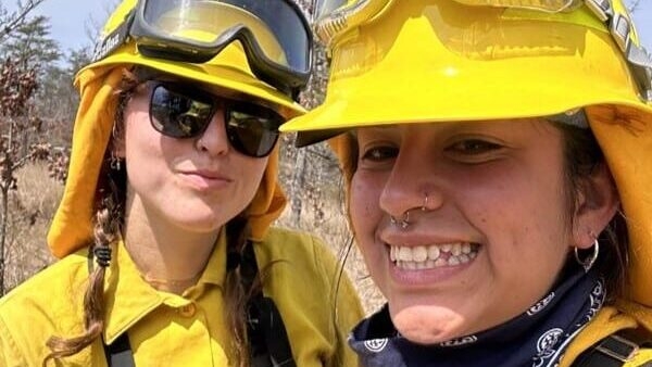 Two young women in yellow protective fire gear smile at the camera