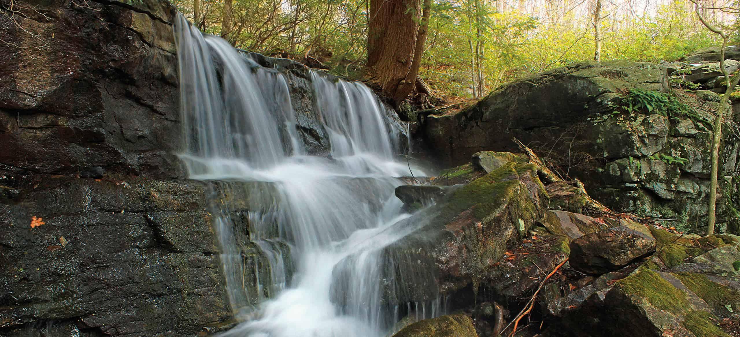 Photo of a cascading, multi-level waterfall down a stony ledge in autumn.