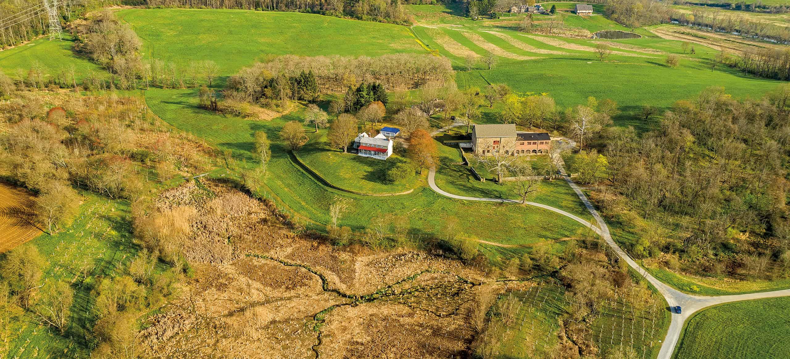 aerial photo of two structures in the middle of various green fields and forested areas