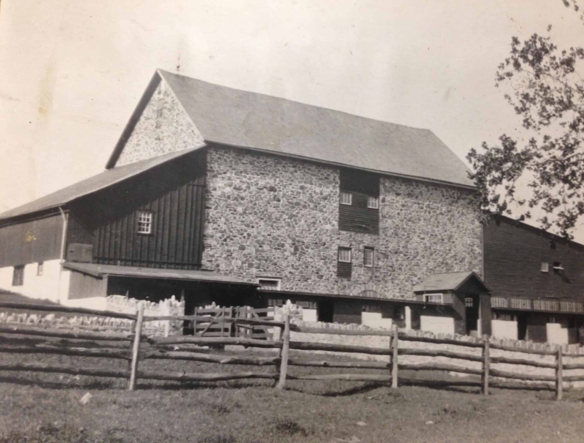 old black and white photo of a stone barn with wooden plank fencing