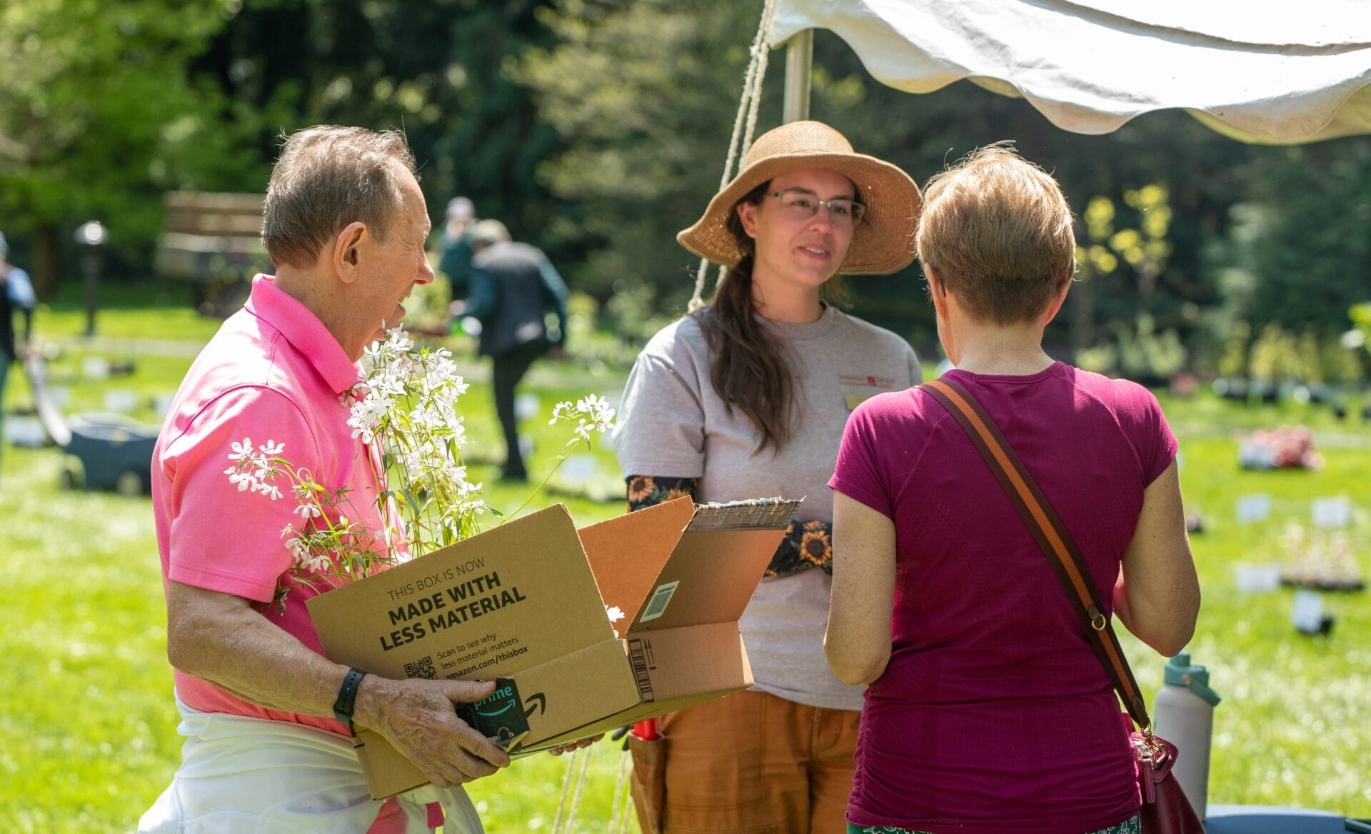 a man carries a box of blooming plants and two women in summer clothes speak to each other