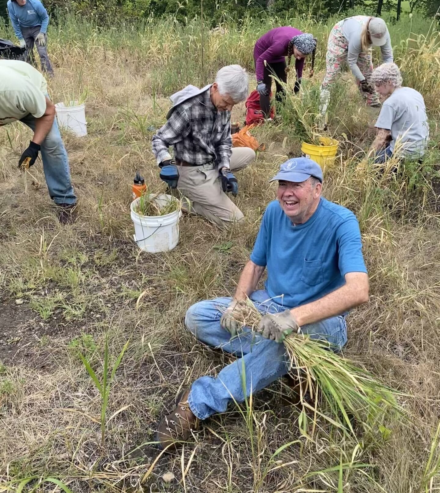 a group of people pulling grasses and a smiling man in foreground