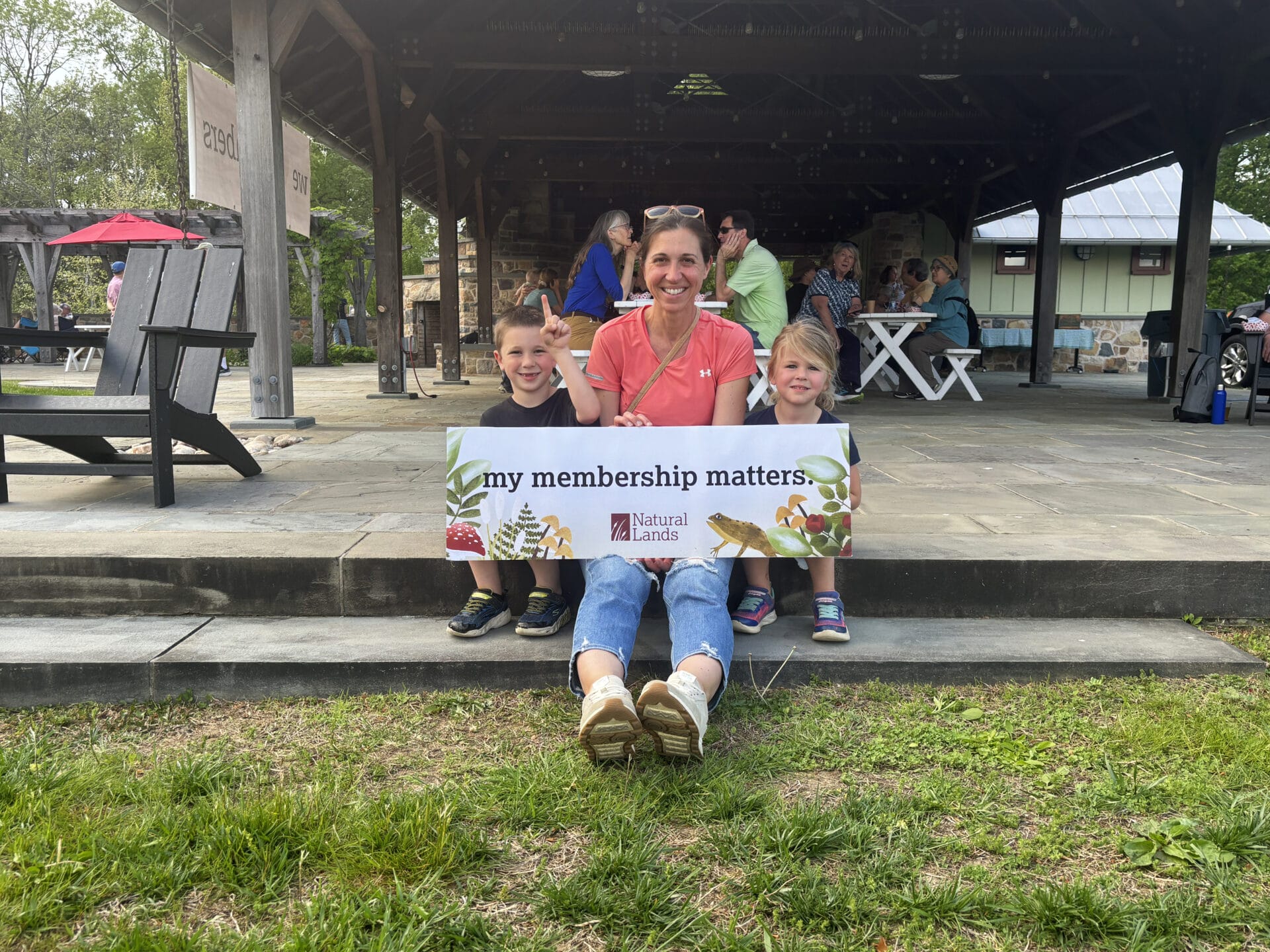 A smiling woman and two children sitting outside holding a sign that says my membership matters.